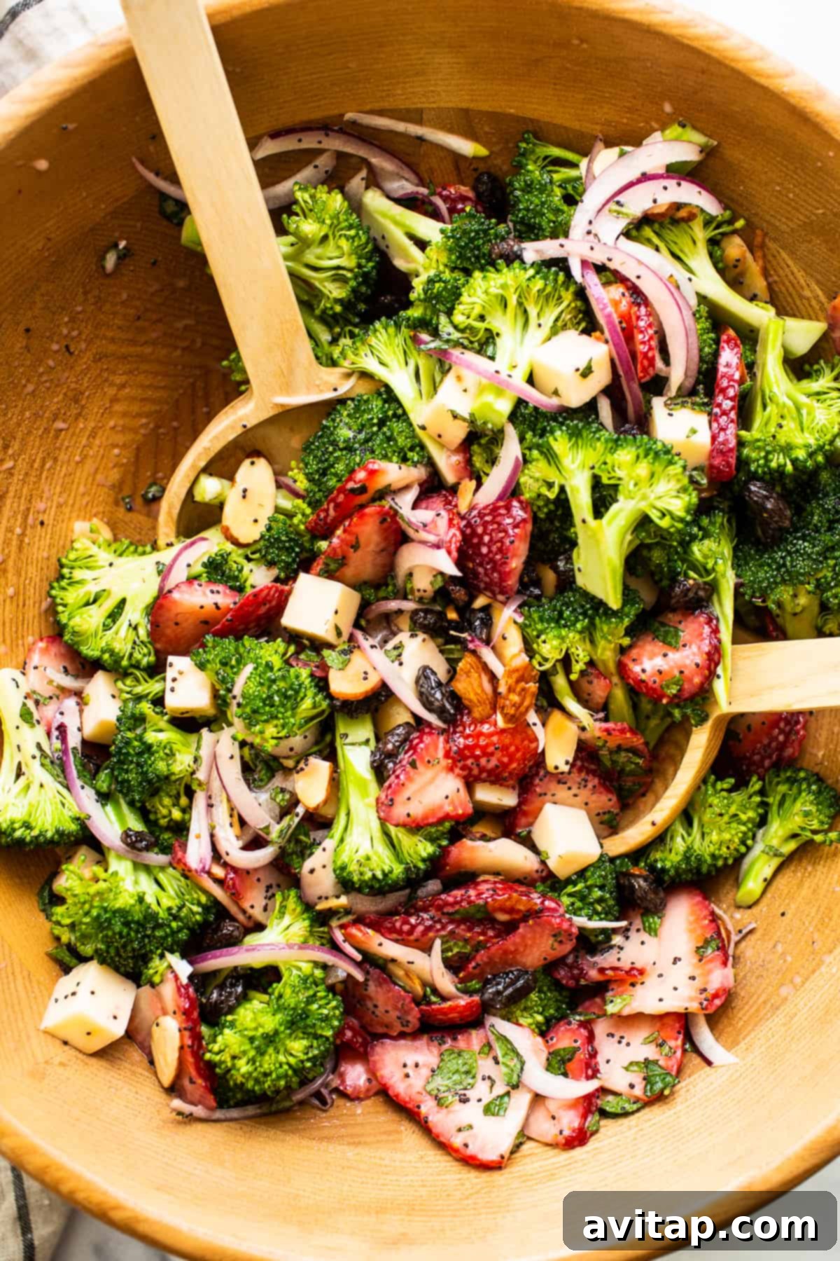 A beautifully presented strawberry broccoli salad in a rustic wooden bowl, ready to be served, garnished with fresh mint.