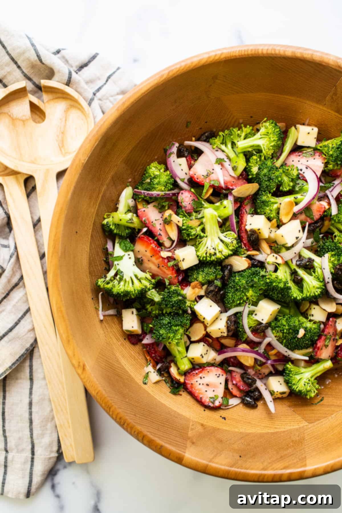 A large wooden bowl filled with vibrant strawberry broccoli salad, garnished with fresh mint leaves, showcasing its fresh and appealing look.