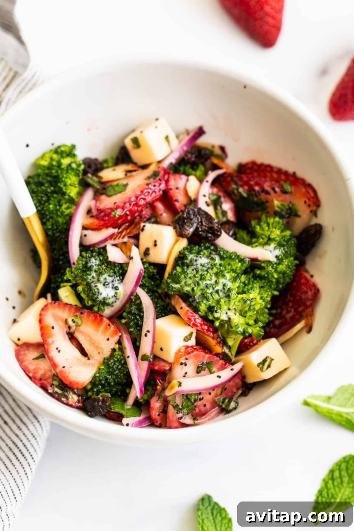 A large bowl of strawberry broccoli salad, with a serving spoon nestled within, ready to be dished out and enjoyed.