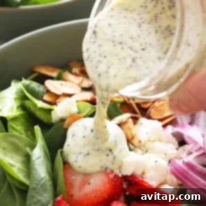 A close-up of a stream of homemade poppy seed dressing being poured over a fresh salad ingredients.