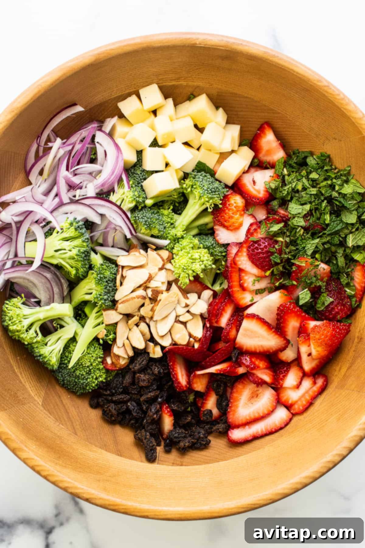 All the vibrant ingredients for strawberry broccoli salad mixed together in a large wooden bowl, waiting for the dressing.