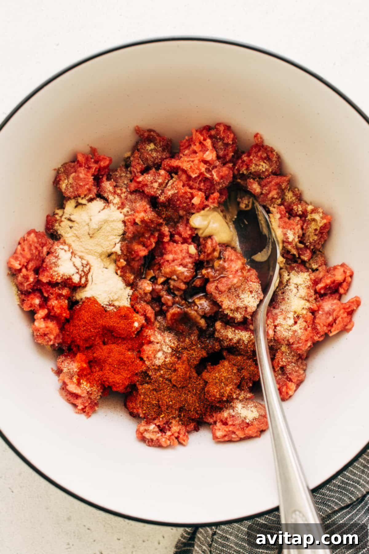 Fresh ingredients for homemade burger patties, including premium ground beef, an assortment of vibrant spices, and a stick of cold butter, neatly arranged in a spacious mixing bowl, eagerly awaiting combination.
