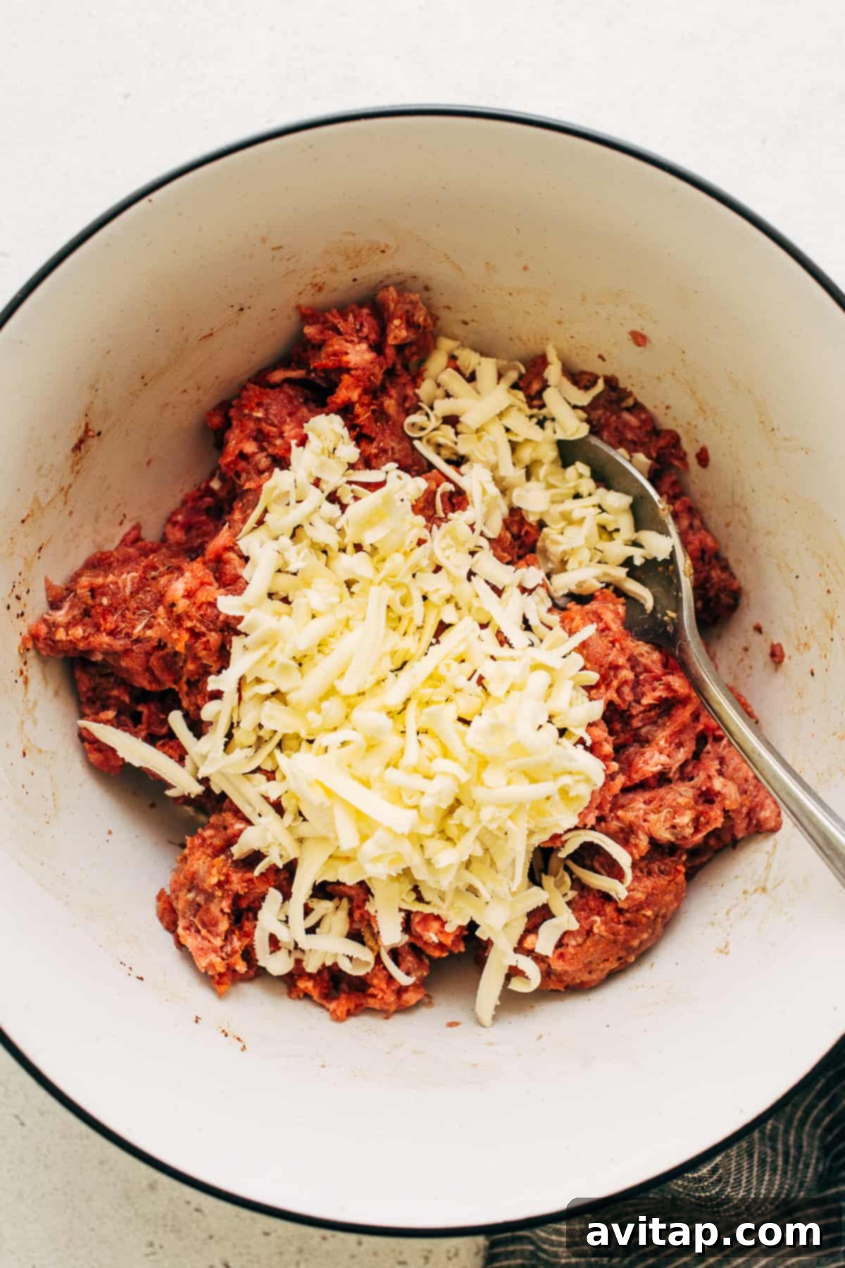 A large mixing bowl containing perfectly seasoned ground beef, generously topped with a mound of freshly grated cold butter, clearly highlighting the key ingredient for achieving ultimate burger juiciness and tenderness.
