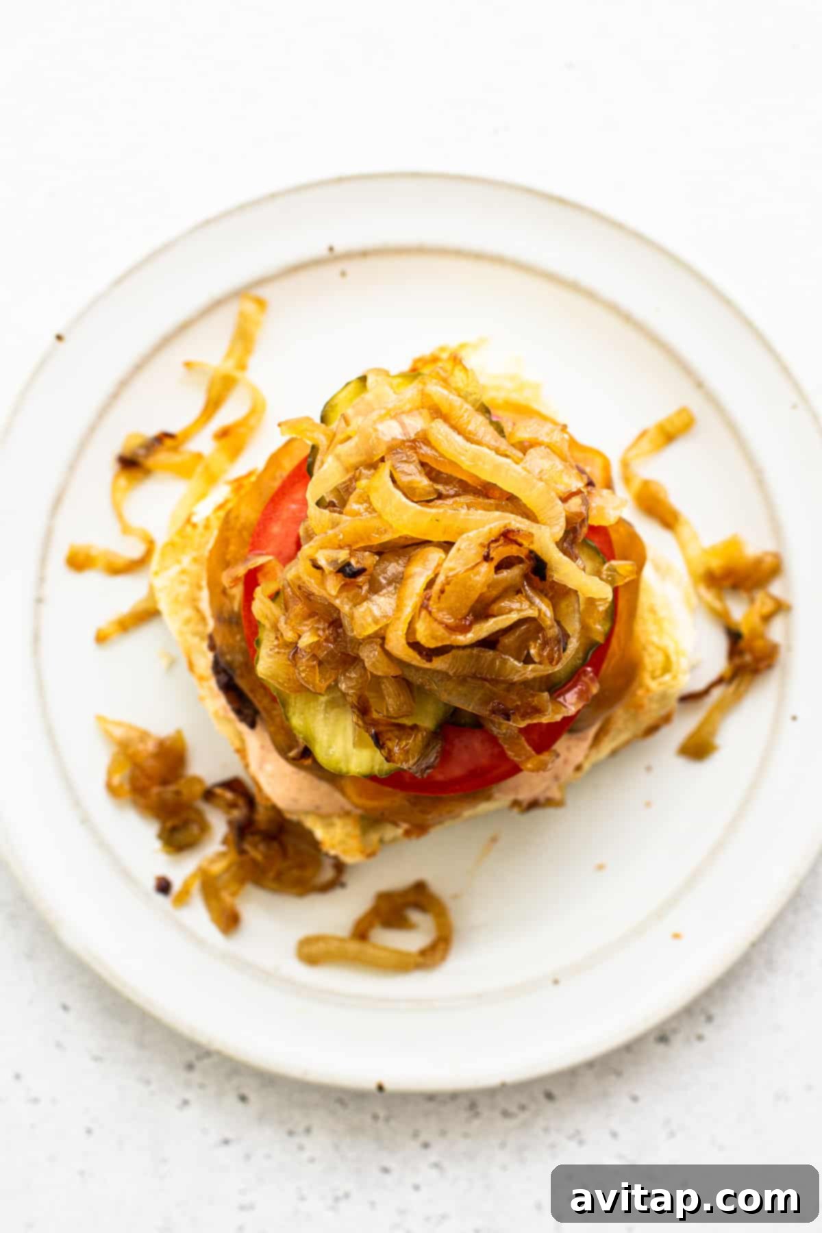 A beautifully assembled homemade burger, generously topped with sweet caramelized onions, crisp dill pickles, and fresh tomato, nestled on a toasted bun and served on a rustic plate, emphasizing its delicious appeal.