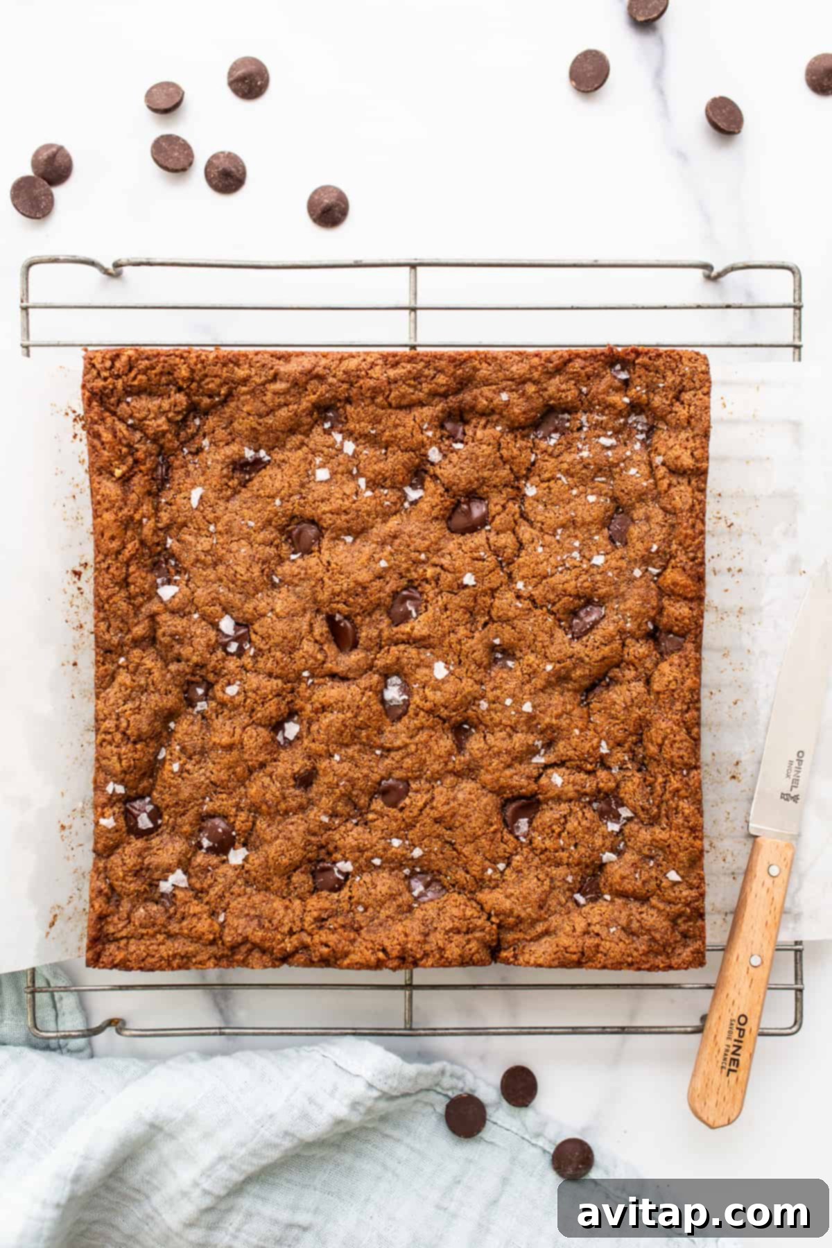 Freshly baked and cooled flourless almond butter chocolate chip cookie bars resting on a wire rack, ready for slicing.