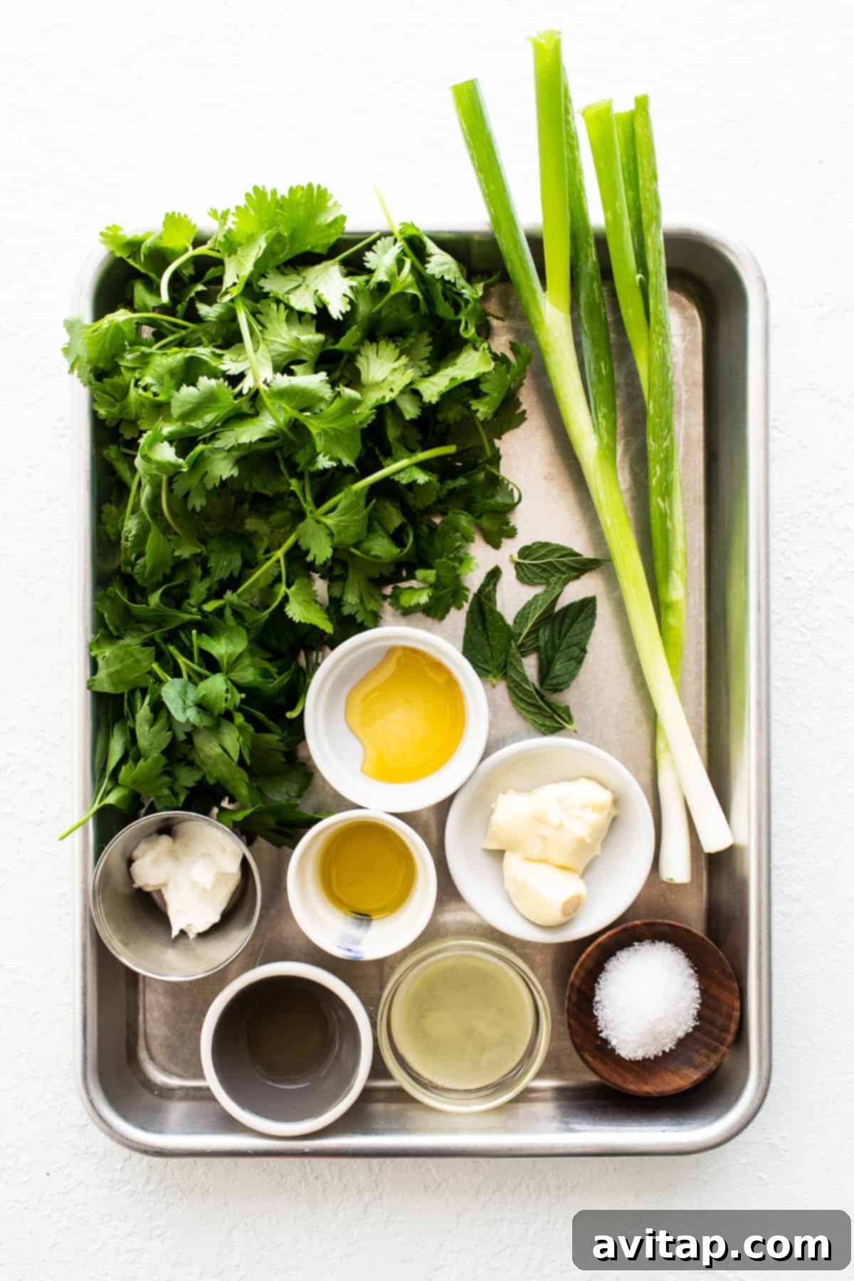 Various fresh ingredients laid out on a baking sheet, ready for green sauce preparation.