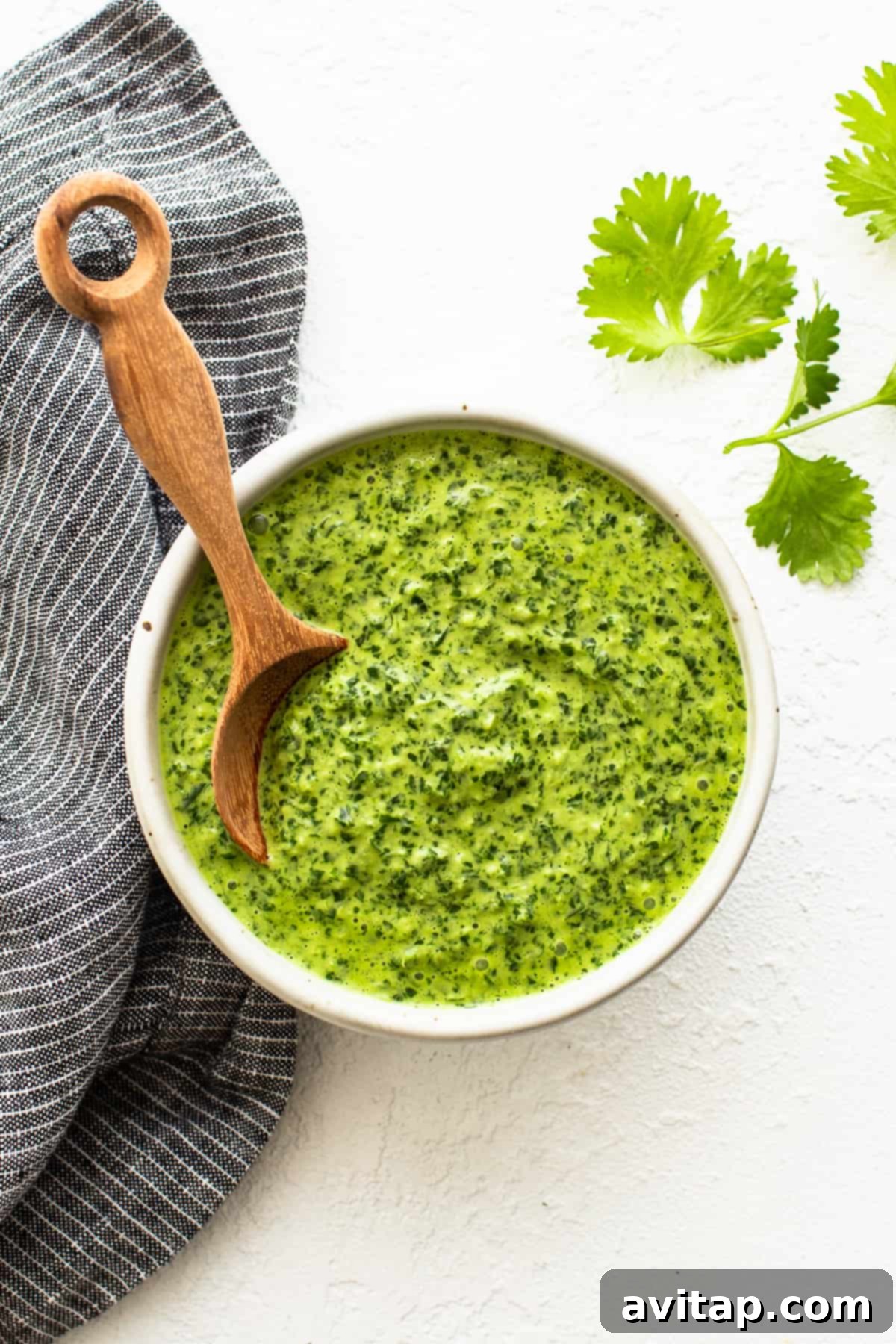 A bowl of vibrant green sauce with a wooden spoon resting in it, ready for serving.