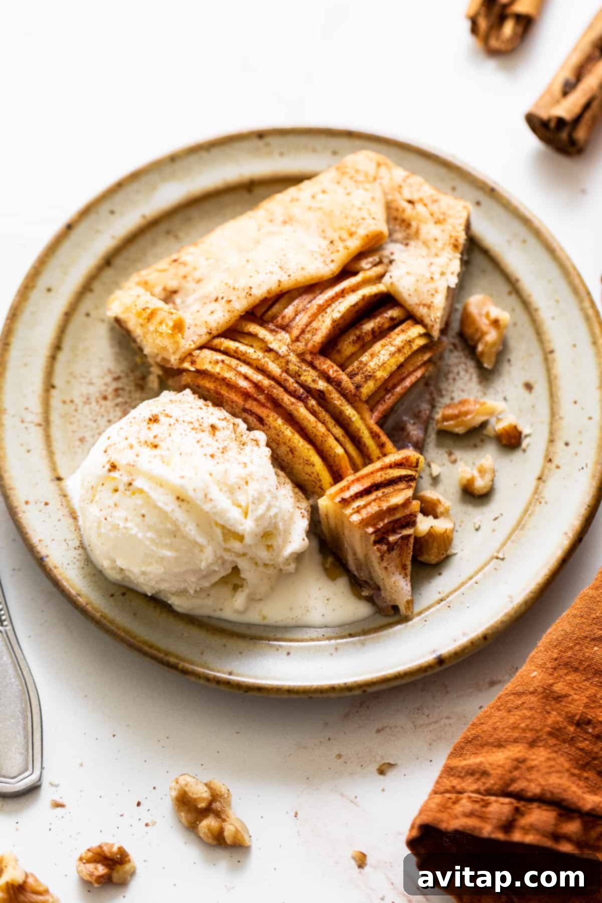 A generous slice of golden-brown apple galette, served warm with a scoop of vanilla ice cream melting delicately on top, showcasing the beautifully arranged apple slices and flaky crust.