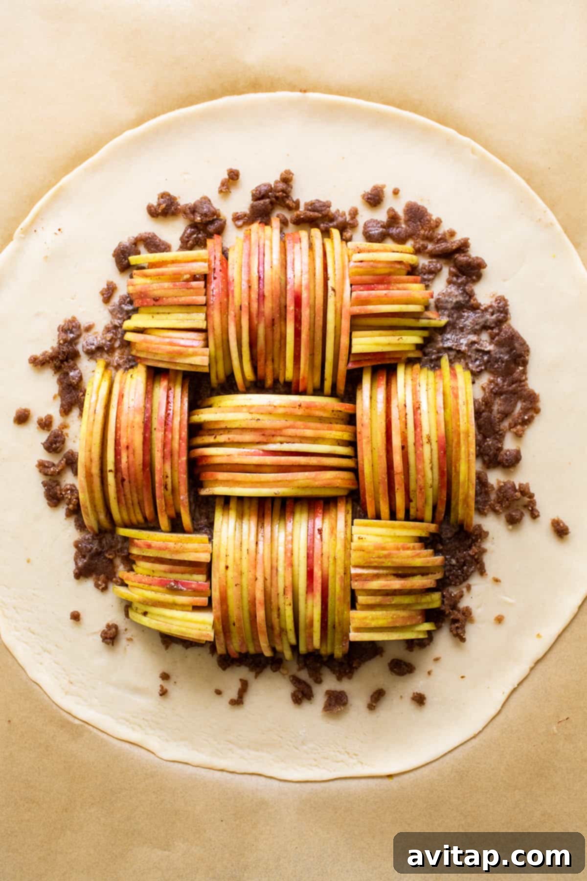 An unbaked apple galette, featuring beautifully layered apple slices and a neatly folded pie crust edge, resting on parchment paper before baking.