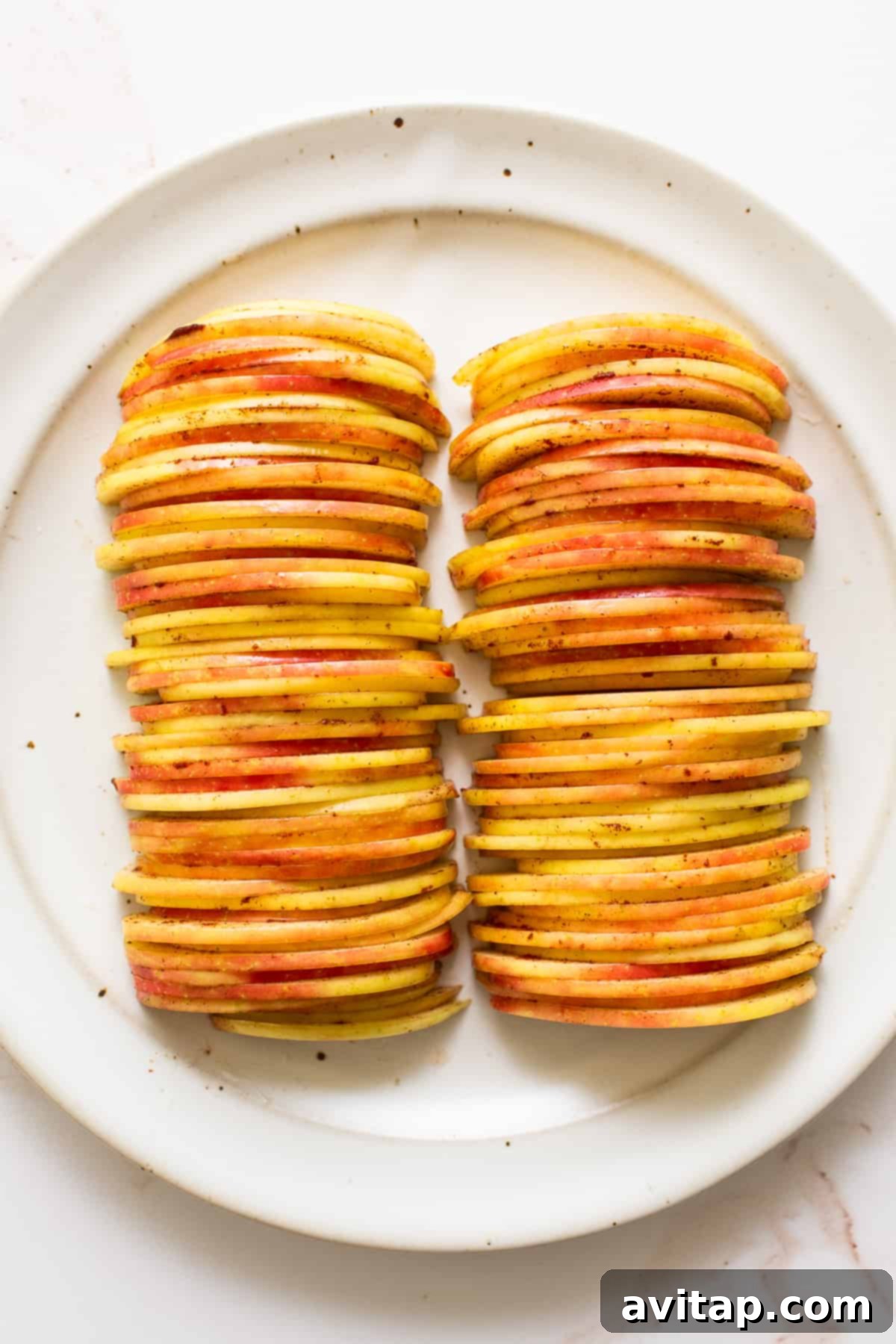 A vibrant bowl of thinly sliced red and green apples, glistening slightly, ready for baking.