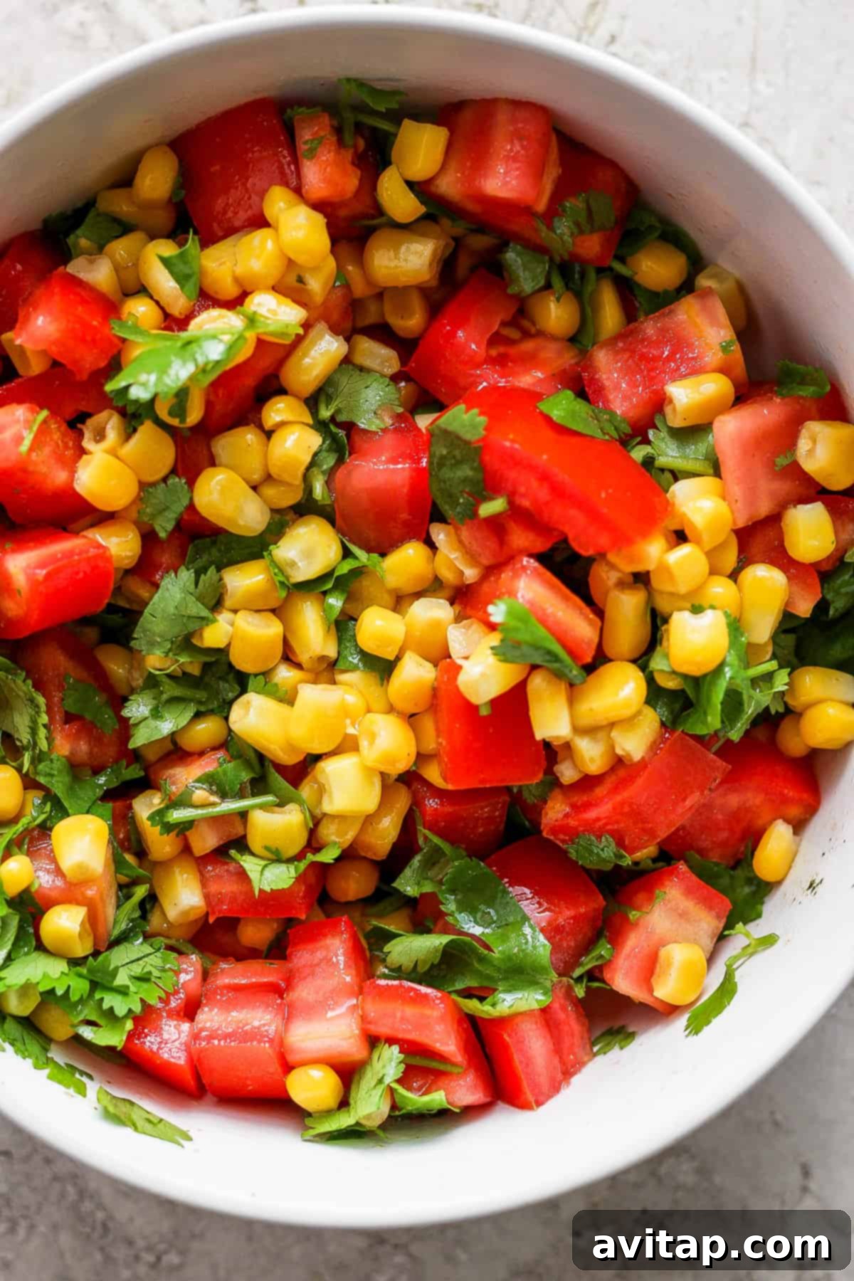 A beautifully composed fresh corn and tomato salad, seasoned with vibrant herbs, glistening and ready to be mixed into a colorful bowl.