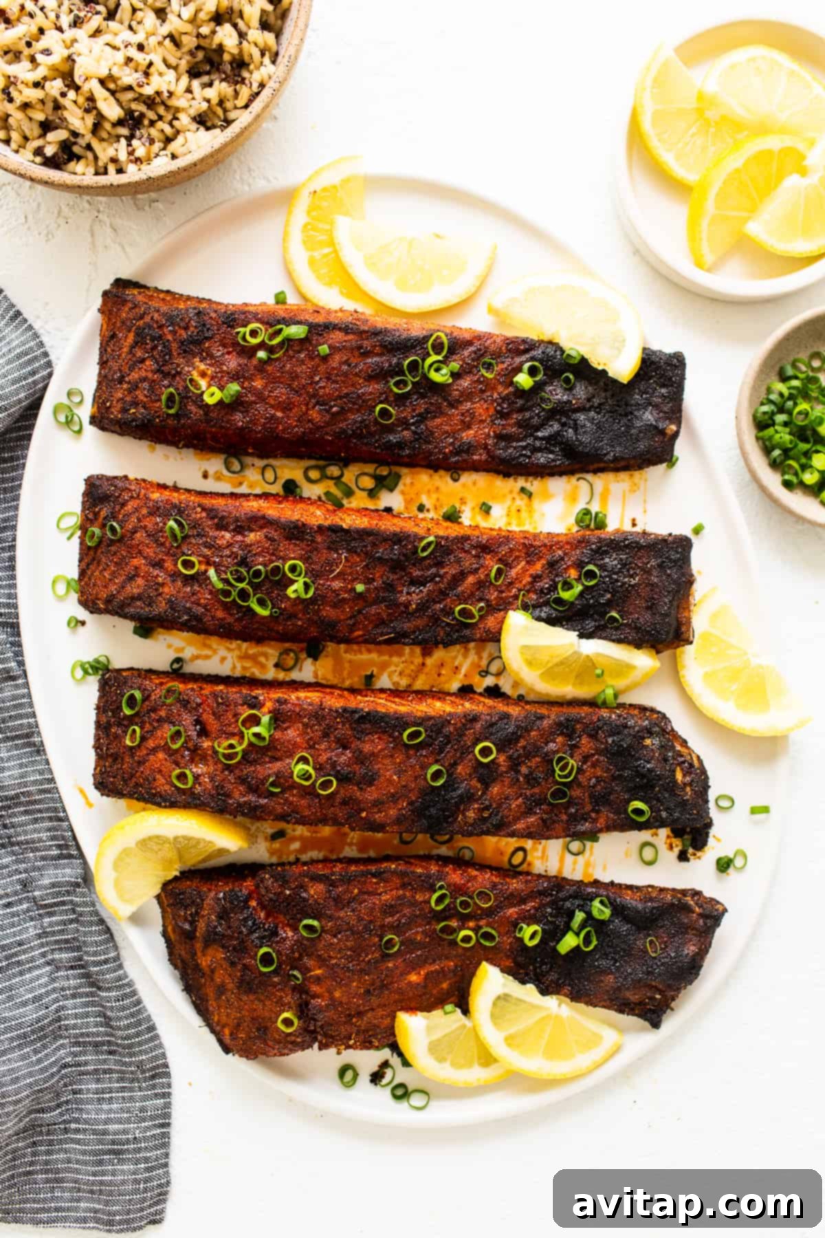 A perfectly broiled blackened salmon fillet, garnished with fresh lemon slices, served on a white plate ready to be enjoyed.