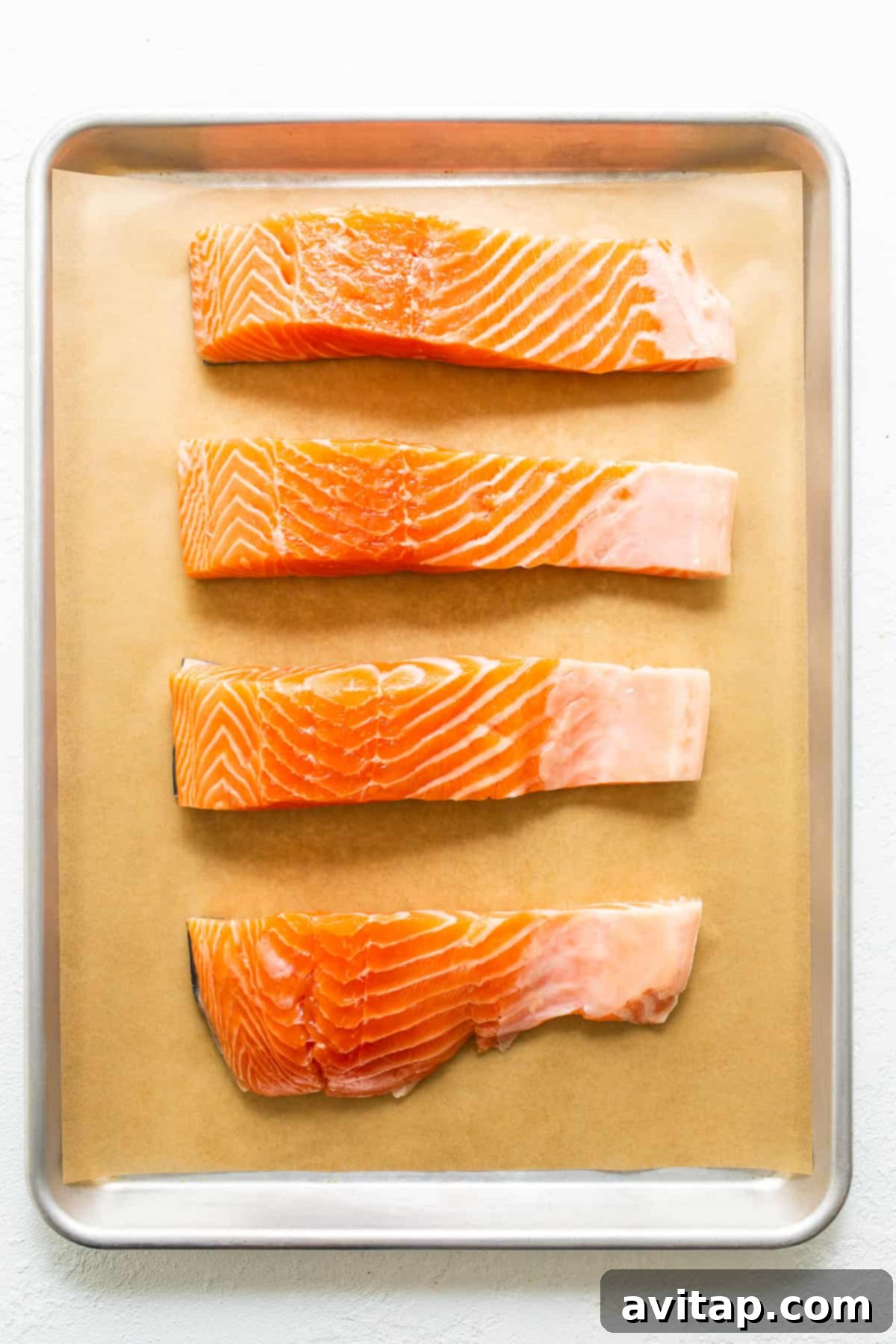 Raw salmon fillets arranged neatly on a baking sheet, ready for seasoning. Emphasizing the importance of choosing similar-sized fillets for even cooking.