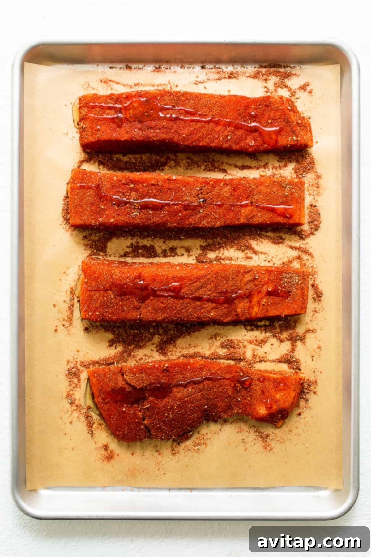 Uncooked salmon fillets coated with Cajun seasoning and drizzled with olive oil, ready for broiling. Highlighting the rich color of the spice rub.
