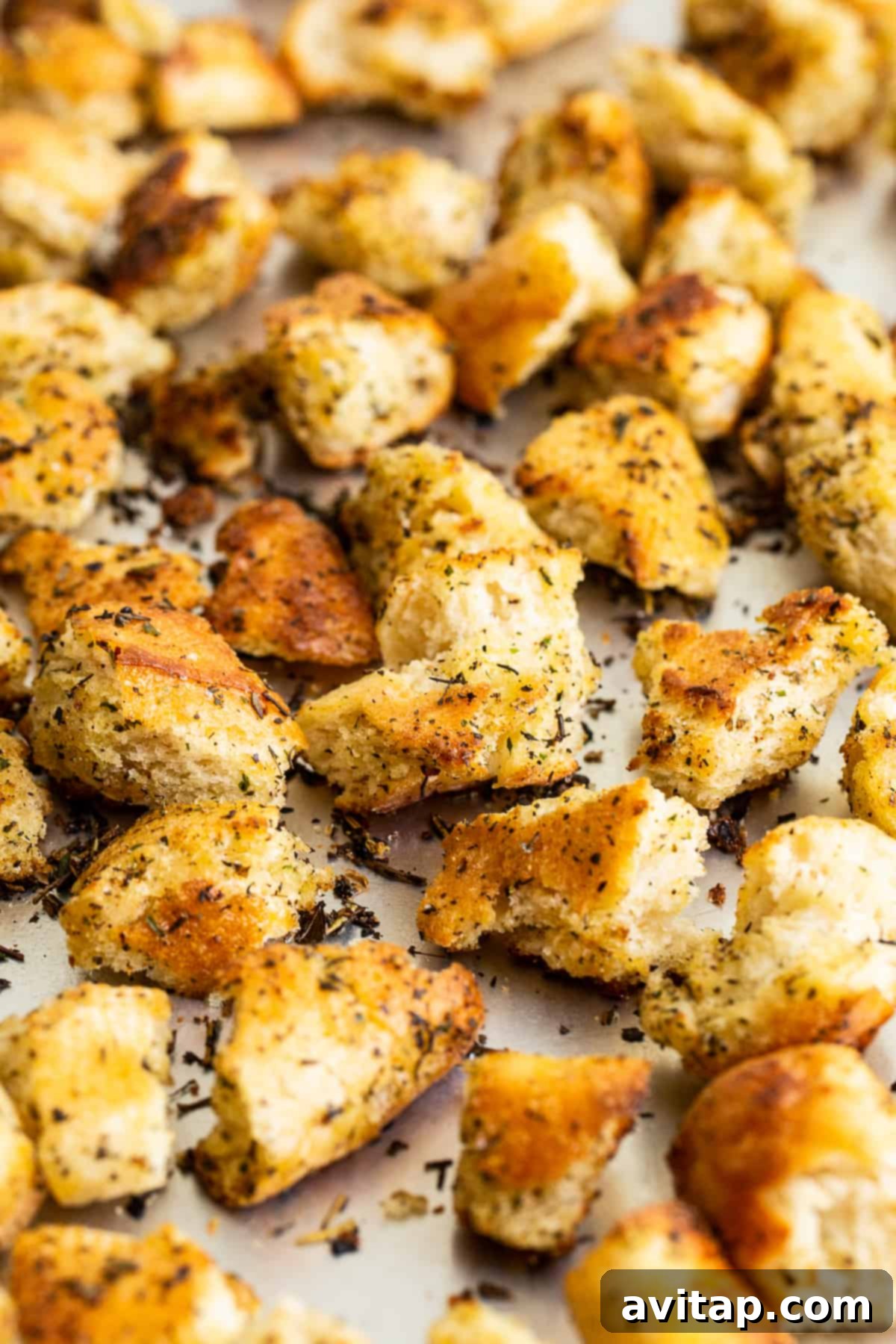 A generous pile of homemade Italian seasoned croutons cooling on a baking sheet after being perfectly pan-fried to a golden-brown finish.