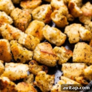 Homemade croutons in a cast iron pan, glistening with olive oil and seasoning, showcasing their golden-brown perfection and appealing texture.