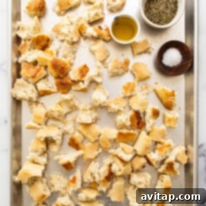 Torn pieces of French baguette spread on a baking sheet, ready for seasoning and frying.