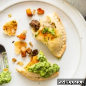 Sweet Potato Ground Beef Empanadas on a plate, garnished with green sauce and fresh herbs.
