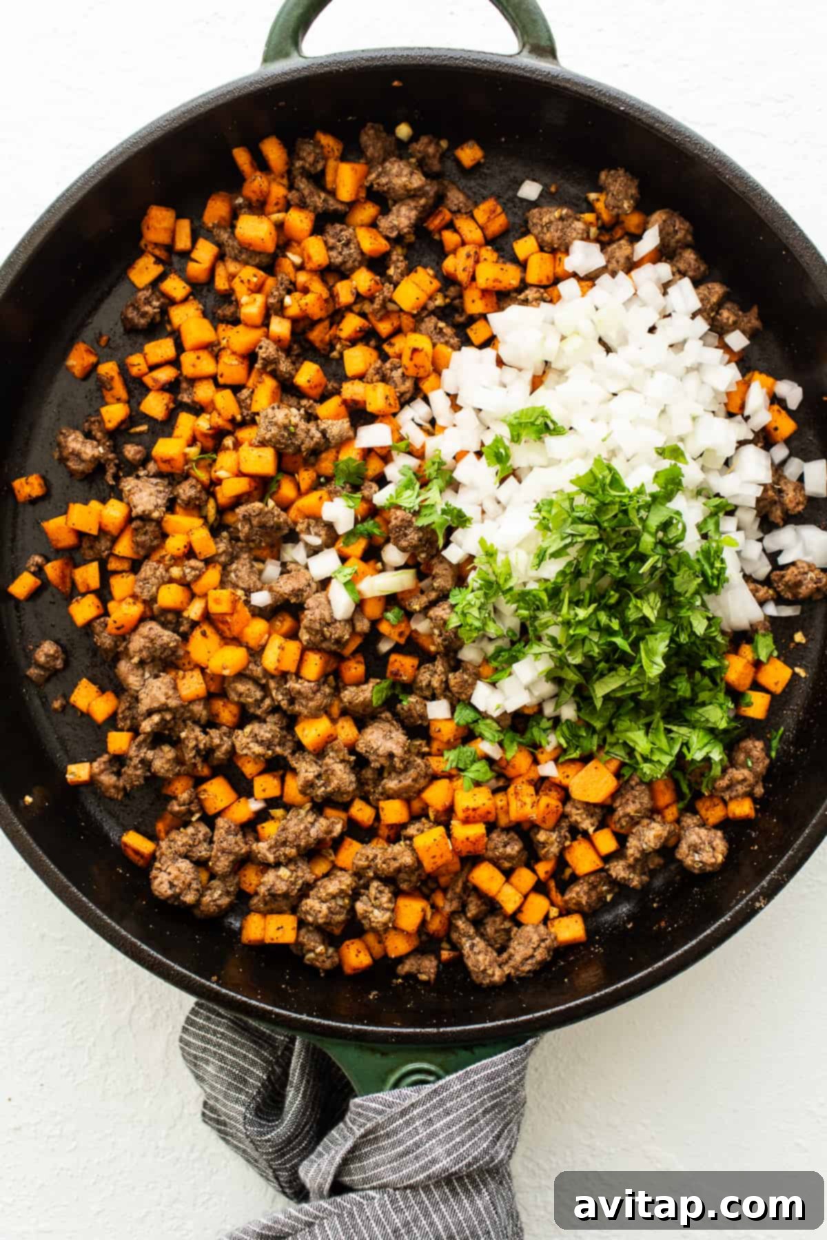 A vibrant mix of ground beef, sweet potatoes, and spices simmering in a skillet, creating a delicious empanada filling.