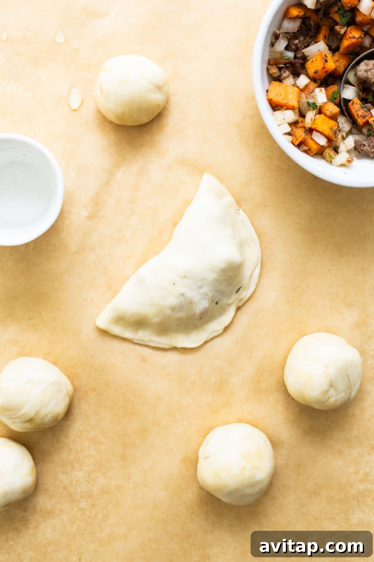 Uncooked sweet potato ground beef empanadas neatly arranged on parchment paper, ready for baking.
