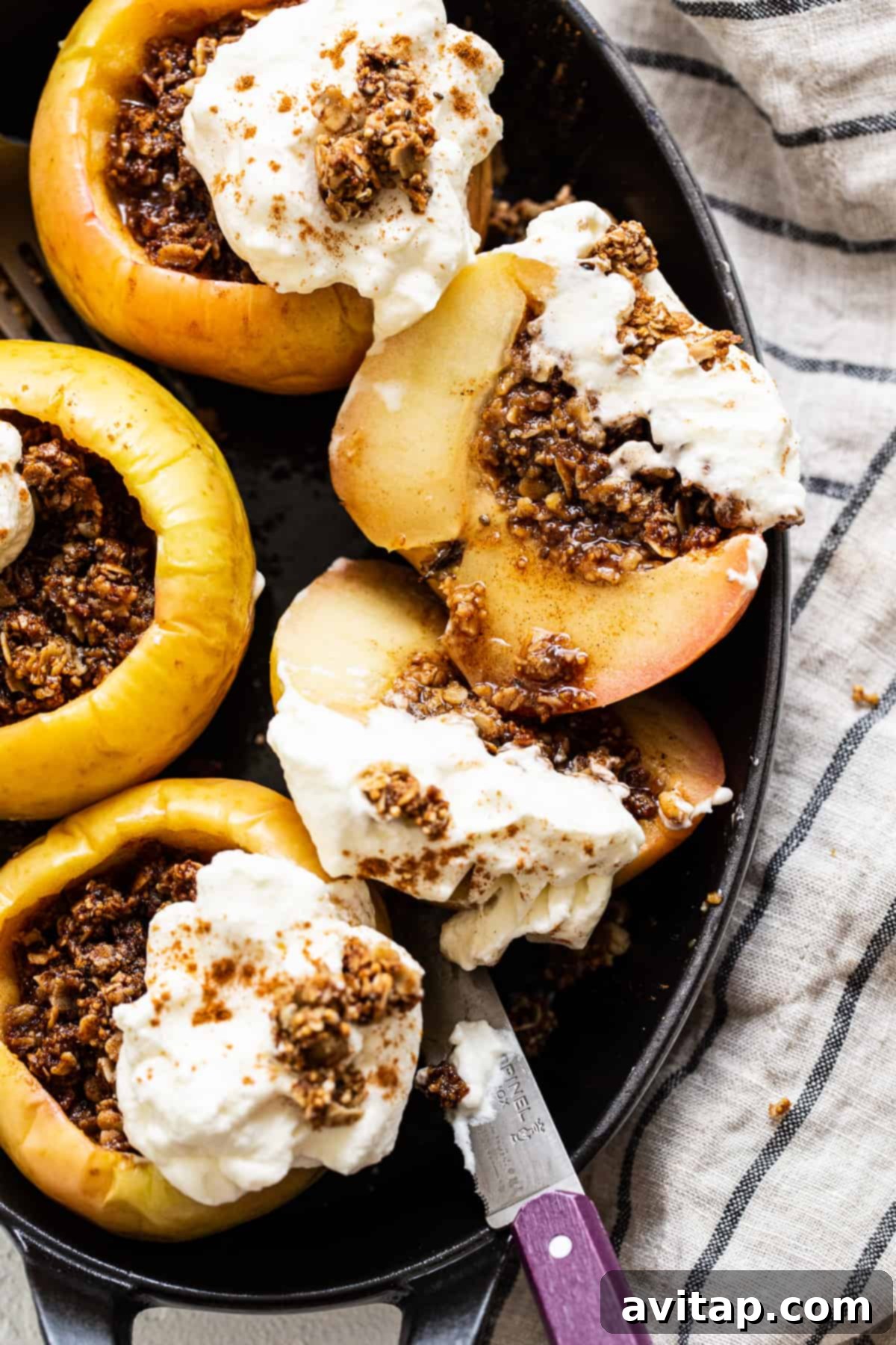 Baked apples topped with whipped cream and a sprinkle of granola, ready to be served.