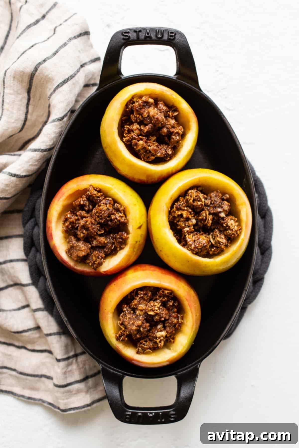Apples filled with granola streusel in a baking dish, ready for their final bake.