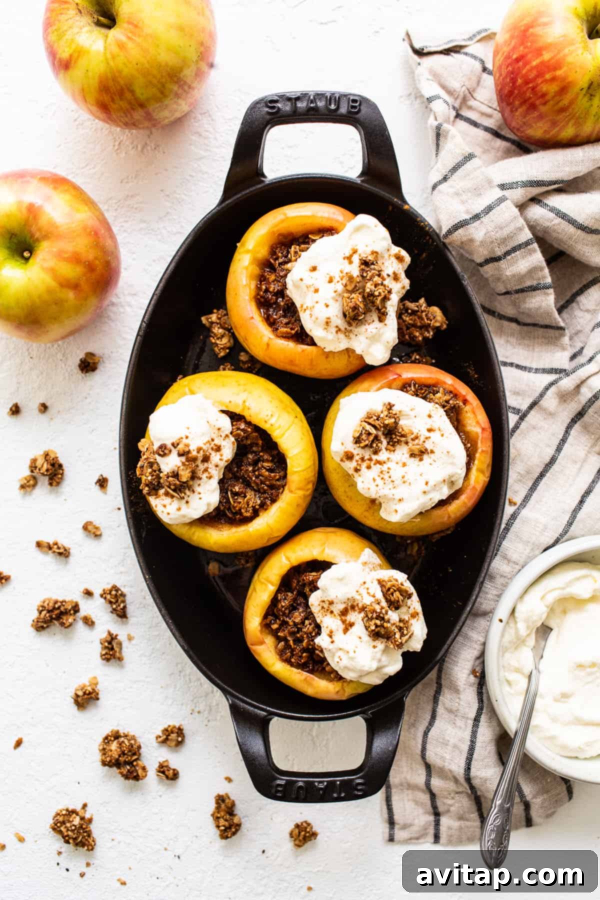 Two baked apples topped with generous swirls of whipped cream, garnished with granola.