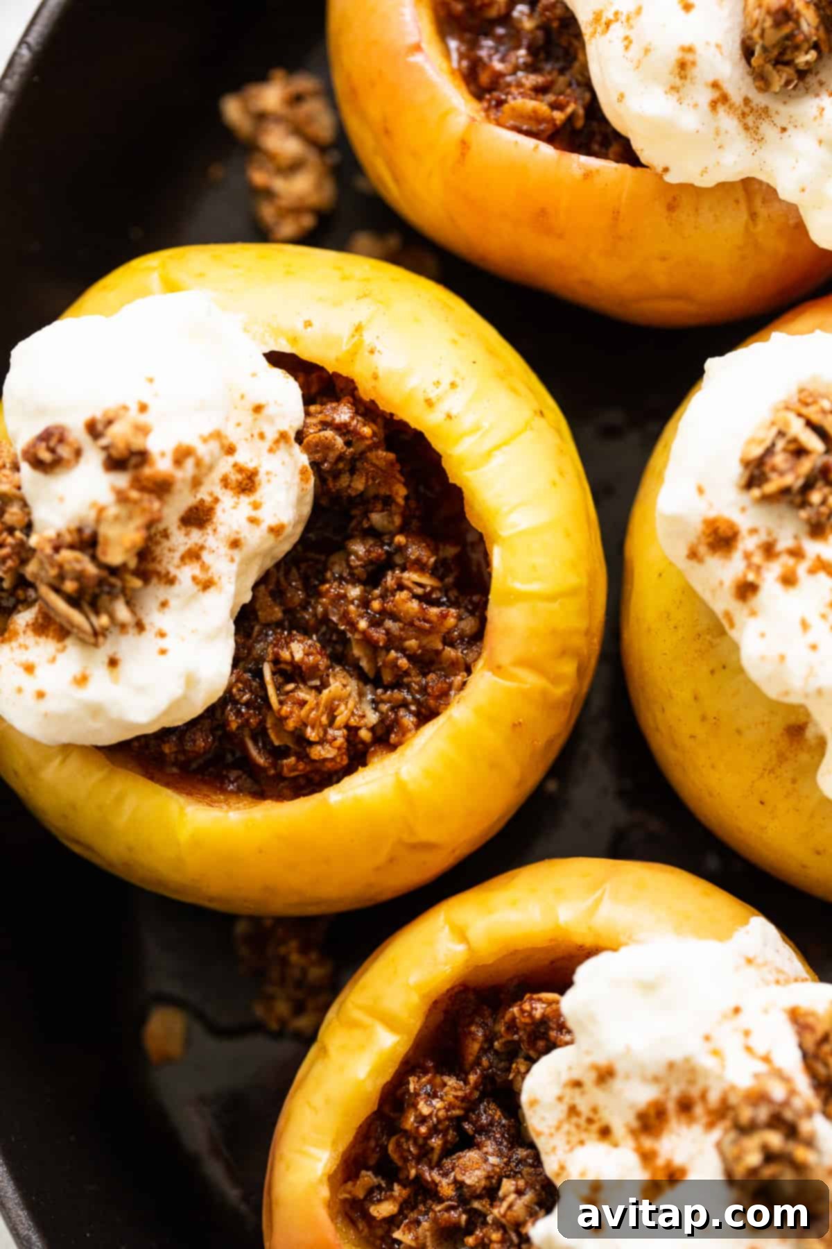 A single baked apple generously topped with whipped cream and a sprinkle of spices.