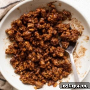 Granola in a white bowl with a spoon, mixed with spices and syrup.