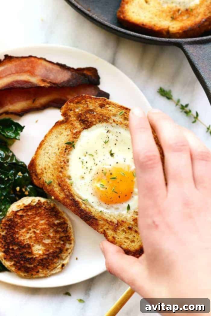 Hand holding egg in toast, showcasing a delicious Eggs in a Basket breakfast.