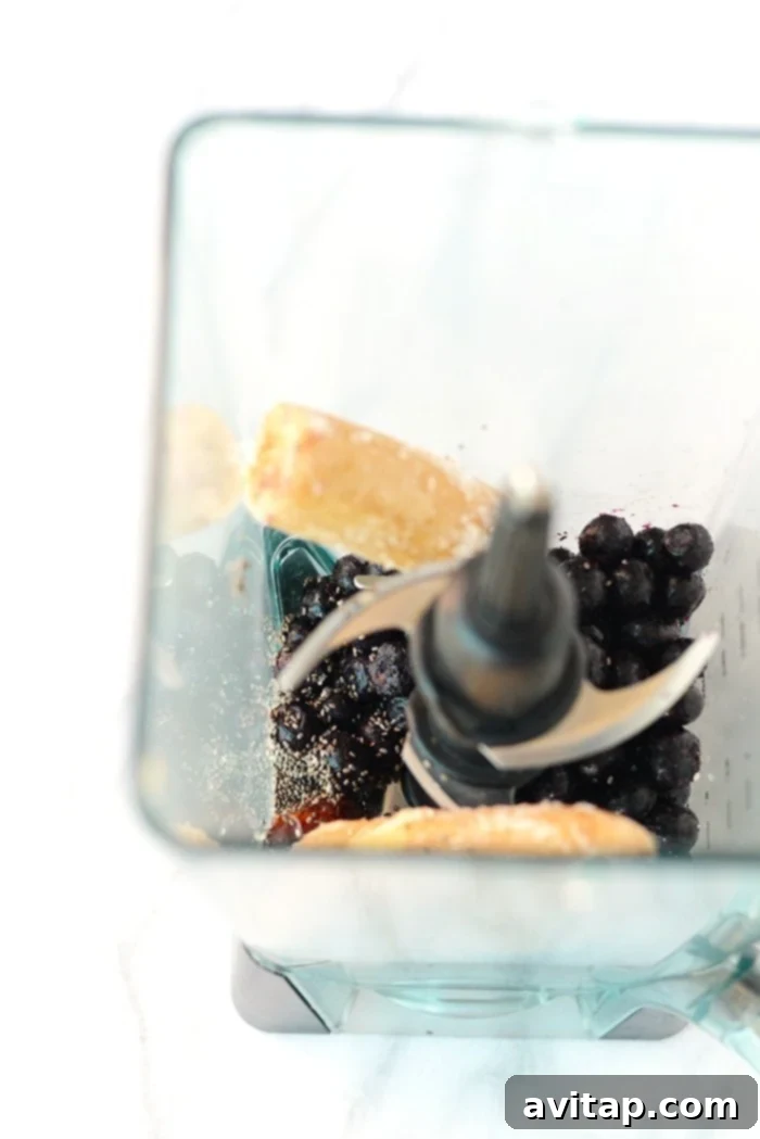 A beautifully presented Blueberry Date Smoothie Bowl, thick and creamy, generously topped with fresh blueberries, slices of kiwi, and shredded coconut for a satisfying and healthy breakfast or snack.
