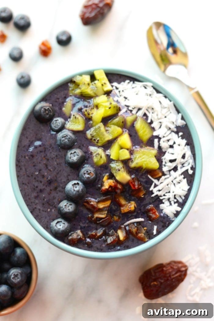 A vibrant Blueberry Date Smoothie Bowl with a spoon, highlighting its creamy texture and fresh fruit toppings, perfect for a quick and healthy meal.
