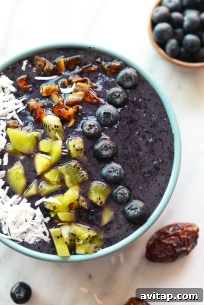 An overhead shot of a vibrant Blueberry Date Smoothie Bowl, laden with colorful toppings like fresh blueberries, sliced kiwi, and crunchy seeds, perfectly arranged for a wholesome and appealing meal.