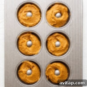 Donut batter being meticulously piped into a donut pan, filling each mold about three-quarters full, demonstrating the precise preparation for baking.
