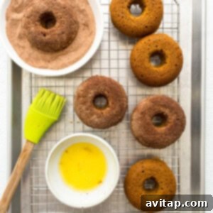 A batch of freshly baked and coated pumpkin donuts cooling on a wire rack, glistening with their cinnamon sugar topping.