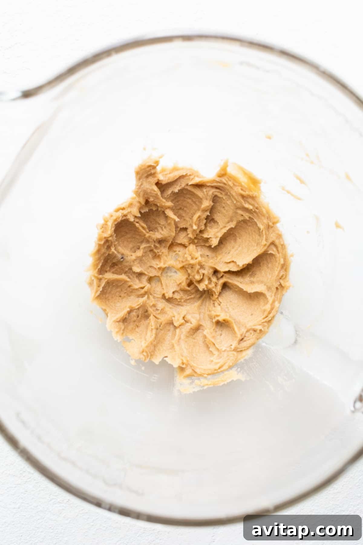 Creaming butter and sugar: the essential first step to unbelievably light and fluffy baked pumpkin donuts. Close-up photo capturing butter and light brown sugar being expertly creamed together in a mixing bowl using an electric mixer, forming a light and fluffy mixture.