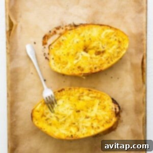 Two baked spaghetti squash boats with a fork preparing to fluff the strands, still on the baking sheet.