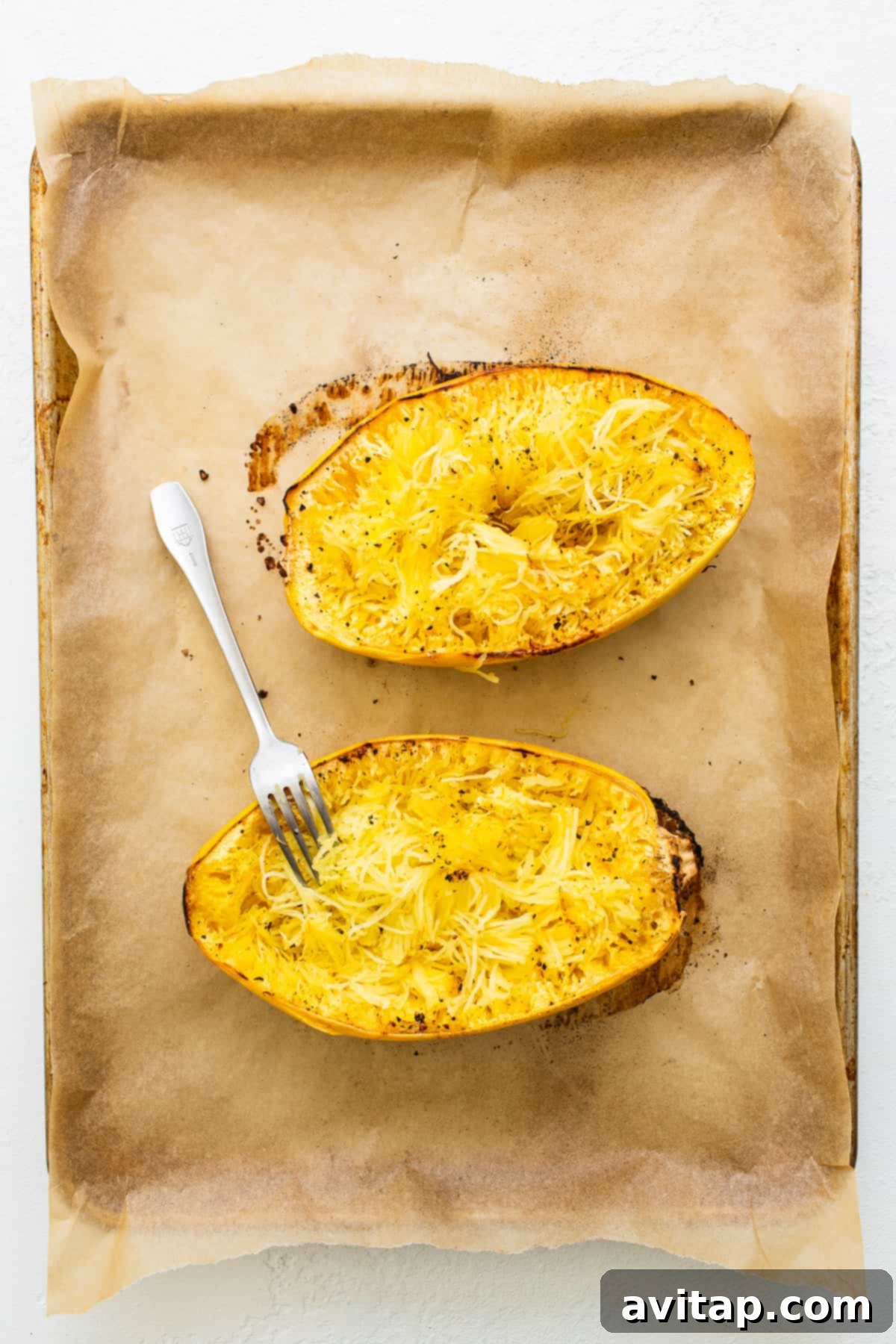 Two halves of seasoned spaghetti squash on a baking sheet, glistening with olive oil and ready for roasting.
