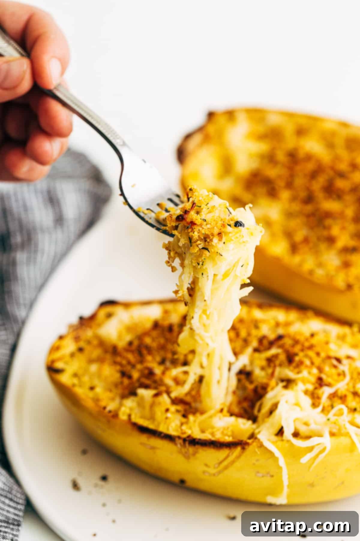 A fork lifting a perfect bite of cheesy spaghetti squash with breadcrumbs from a serving bowl.