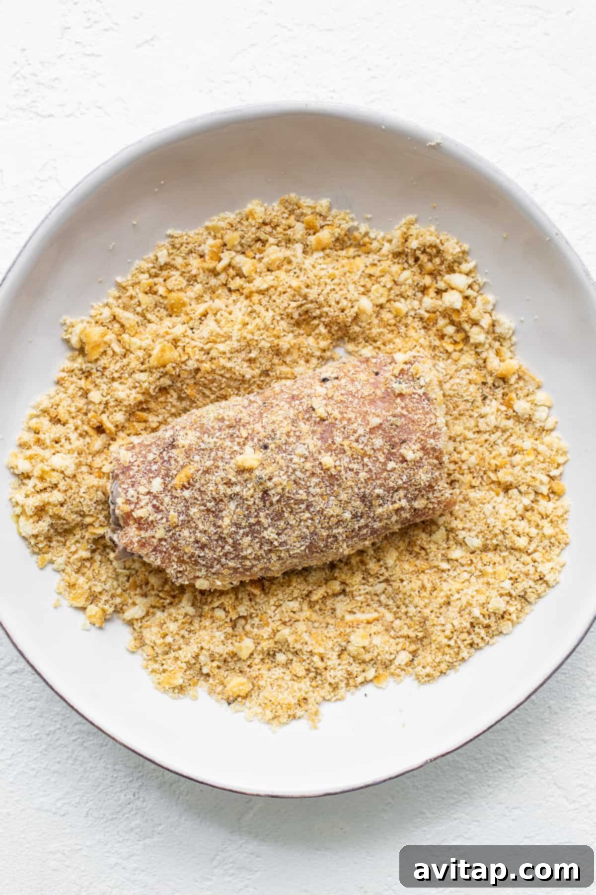 Achieving the Perfect Crunch: Dredging Stuffed Pork Chops Close-up of a hand dredging a stuffed pork chop in Ritz cracker crumbs.