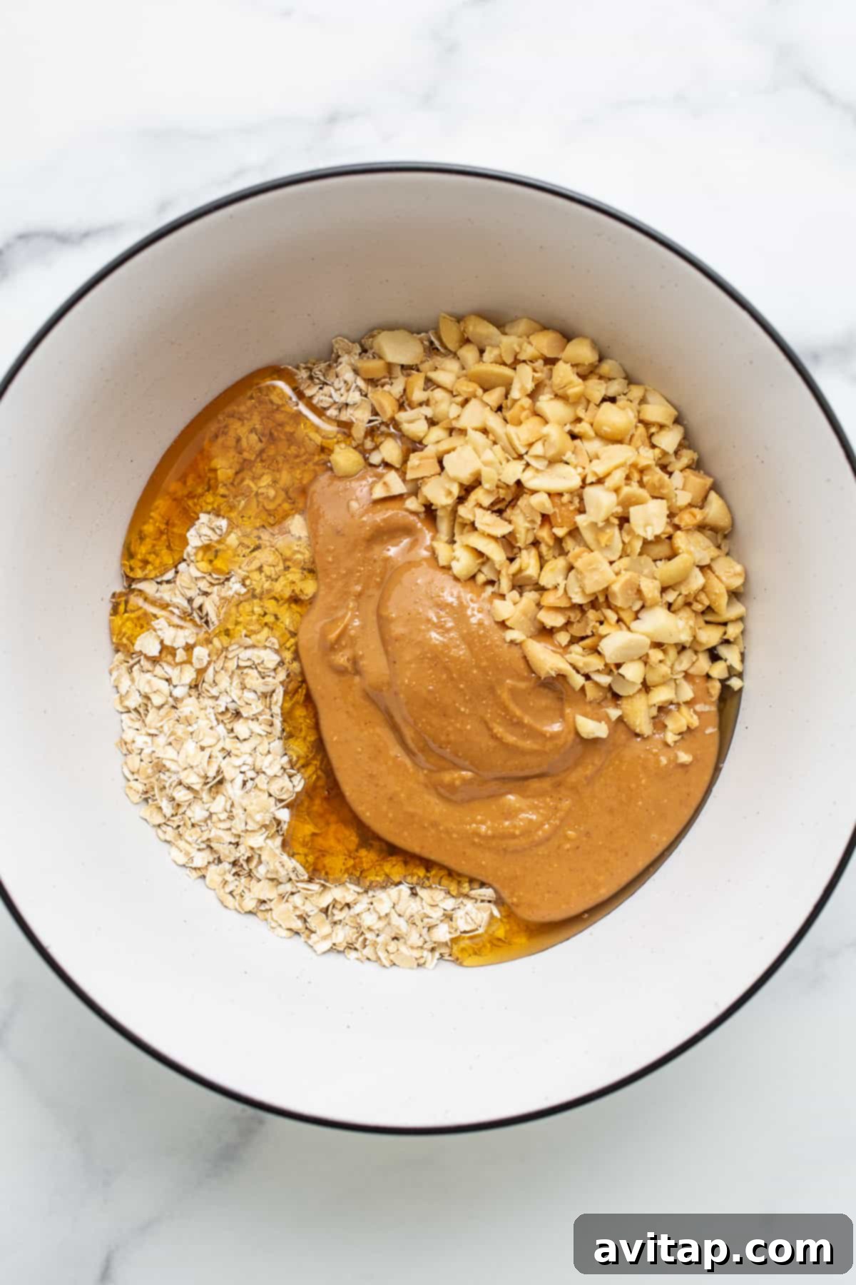 A bowl filled with the base ingredients for oat cups: oats, honey, and peanuts, ready for mixing.
