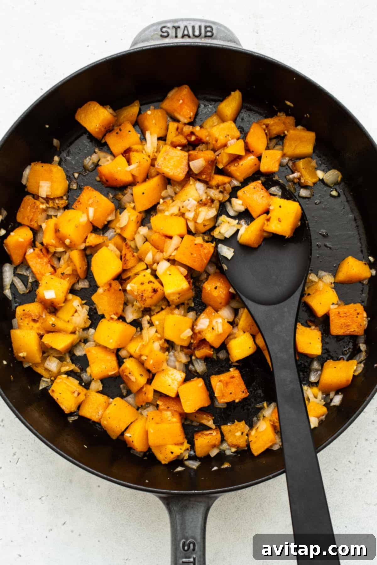 Butternut squash cooking in a pan with aromatic ingredients.