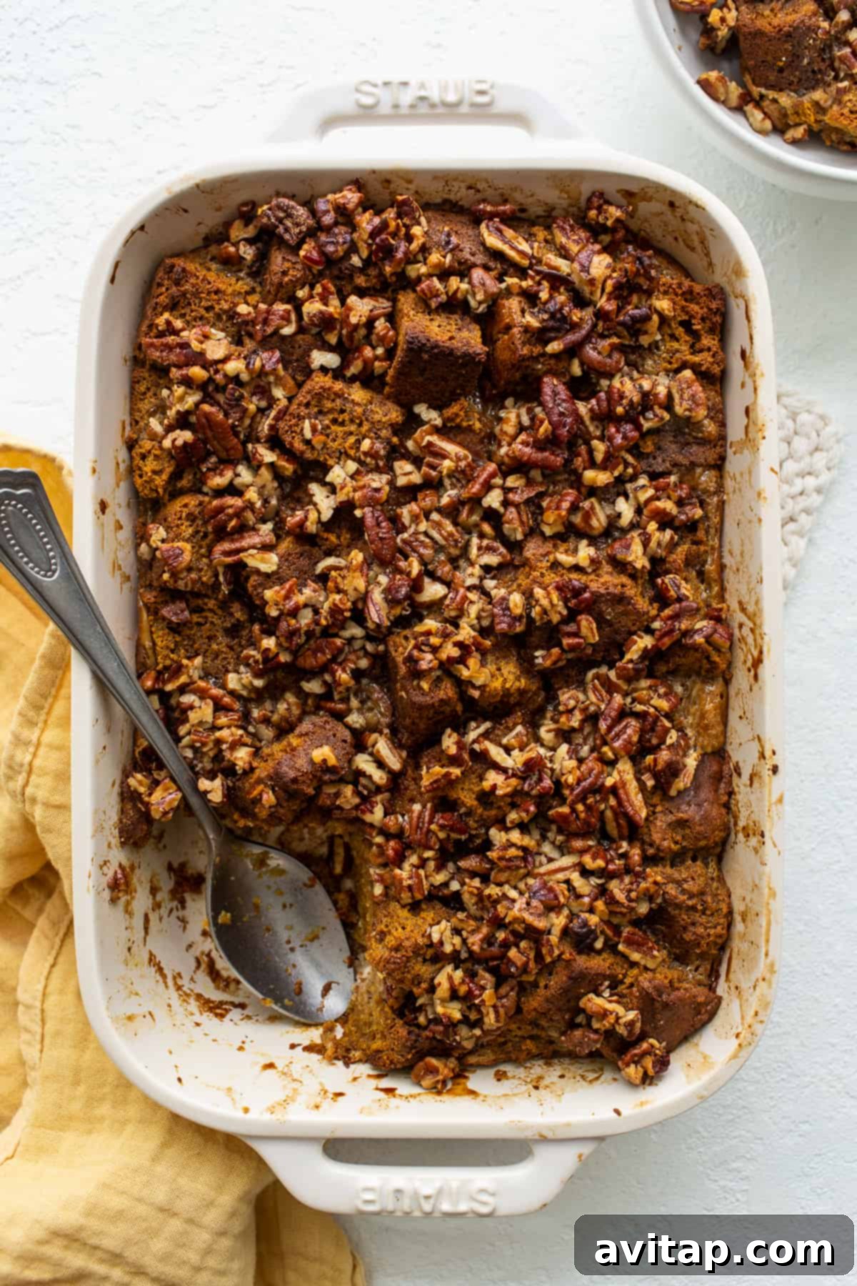 Pumpkin bread pudding in a rustic casserole dish, topped with a dollop of cream.