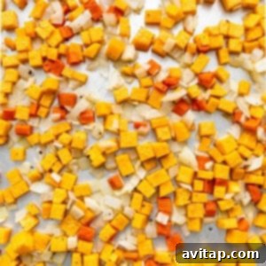 A pile of yellow and orange cubes (butternut squash and carrots) on a baking sheet, ready for roasting.