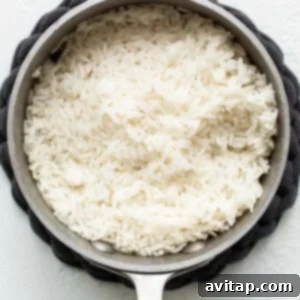 Fluffy white rice resting in a pan on a white background, freshly cooked.