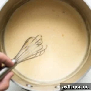 A person whisking a creamy sauce in a pan, creating a smooth roux for the casserole.