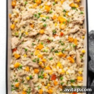 Chicken fried rice, mixed with carrots and peas, being combined in a baking dish.