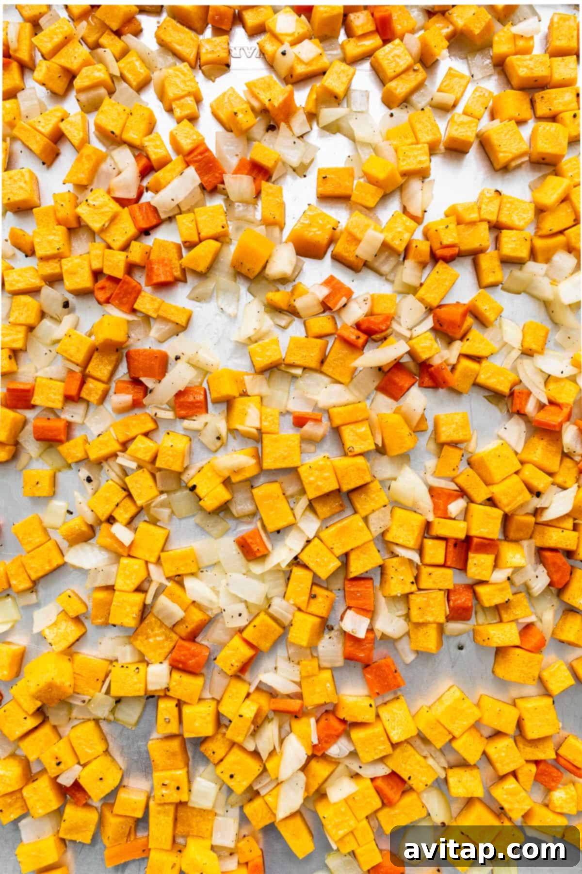 Roasted butternut squash, carrots, and yellow onions on a baking sheet, glistening with olive oil and seasonings.
