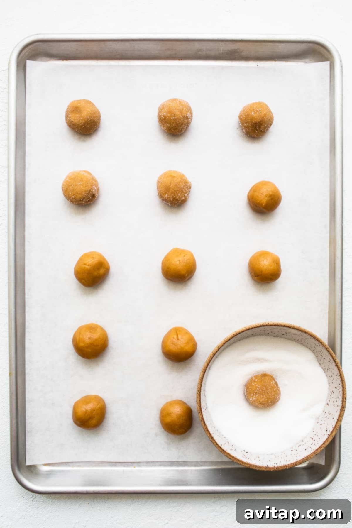 Ready to Bake: Sugar-Coated Cookie Dough Balls Perfectly rolled peanut butter kiss cookie dough balls coated in sugar on a parchment-lined baking sheet.