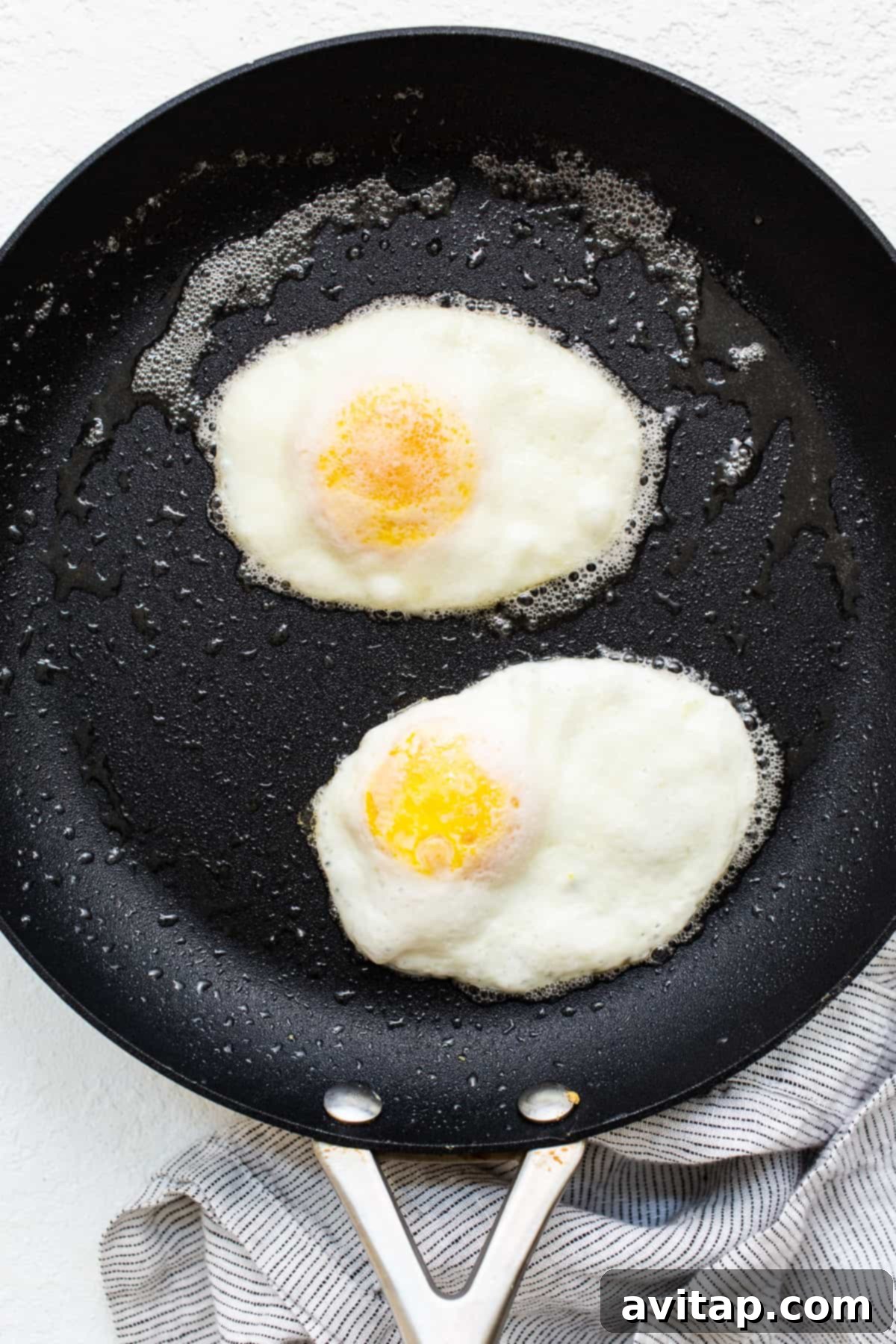 Two over hard eggs cooking in a skillet, with a generous amount of melted butter creating a rich, flavorful cooking environment.